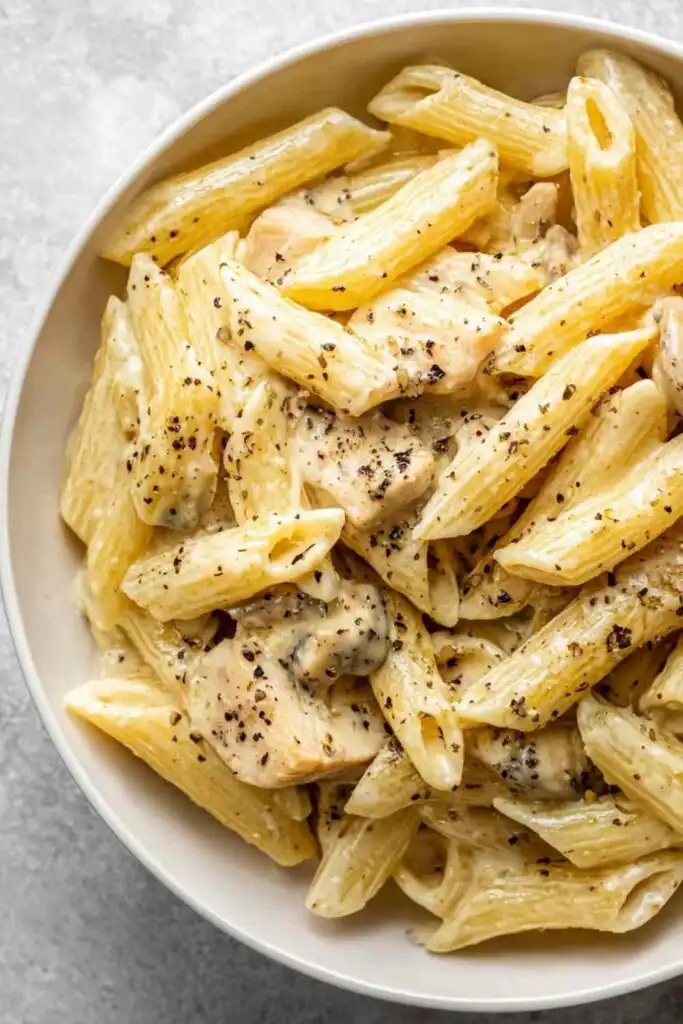 Instant Pot cheesy chicken pasta served in a white bowl topped with freshly grated cheddar and parsley