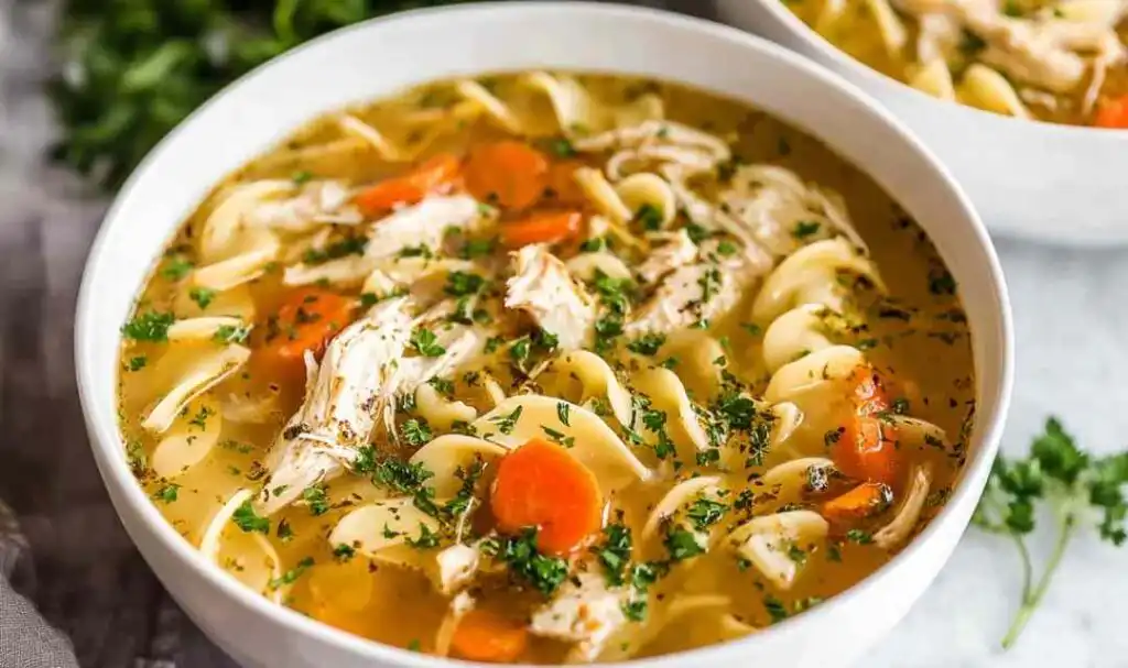 Instant Pot chicken noodle soup in a white bowl with shredded chicken, egg noodles, carrots, and fresh parsley
