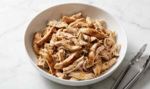 Instant Pot shredded chicken in a white bowl garnished with fresh parsley on a wooden cutting board