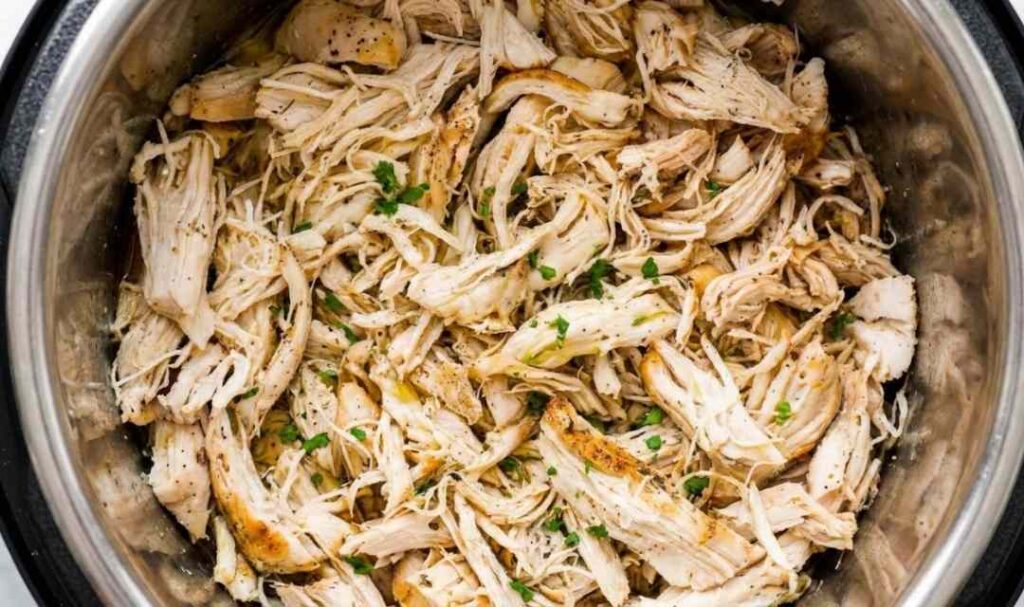 Instant Pot shredded chicken in a white bowl garnished with fresh parsley on a wooden cutting board