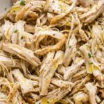 Instant Pot shredded chicken in a white bowl garnished with fresh parsley on a wooden cutting board