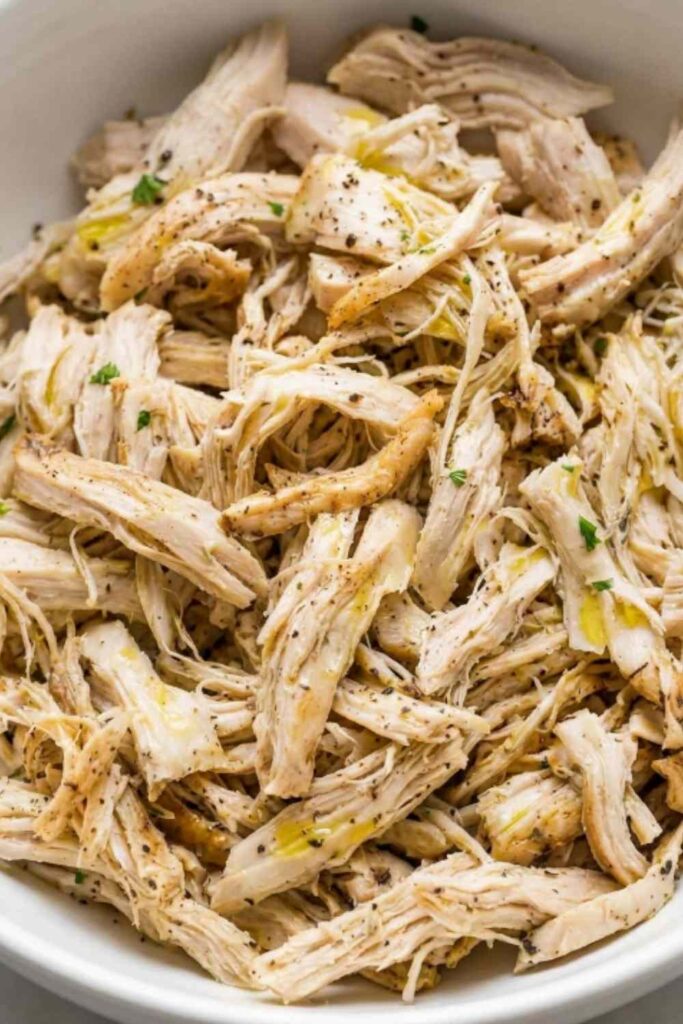 Instant Pot shredded chicken in a white bowl garnished with fresh parsley on a wooden cutting board