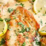 Lemon Parmesan chicken cutlets in a creamy lemon Parmesan sauce garnished with lemon slices and fresh parsley in a skillet