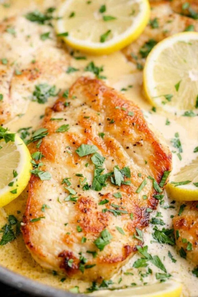 Lemon Parmesan chicken cutlets in a creamy lemon Parmesan sauce garnished with lemon slices and fresh parsley in a skillet
