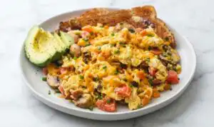 Loaded scrambled eggs with bacon, sauteed bell pepper, mushrooms, and melted cheddar in a nonstick skillet