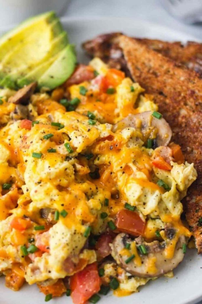 Loaded scrambled eggs with bacon, sauteed bell pepper, mushrooms, and melted cheddar in a nonstick skillet