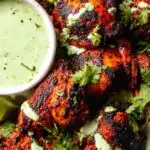 Juicy Peruvian chicken thighs drizzled with creamy cilantro green sauce on a serving platter
