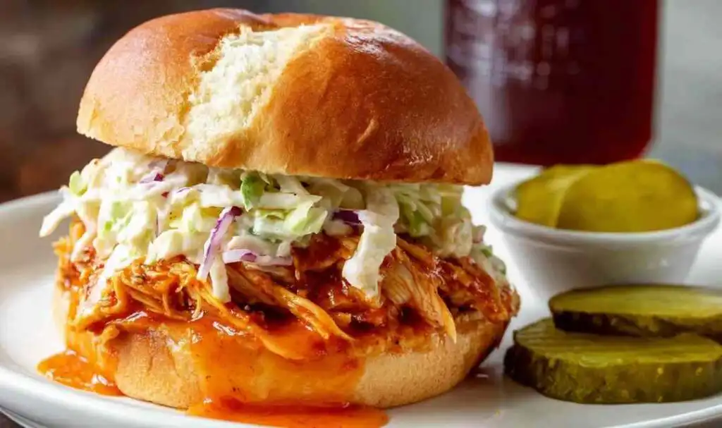 BBQ chicken sandwich with creamy coleslaw and bread and butter pickles on a toasted brioche bun