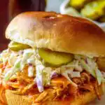 BBQ chicken sandwich with creamy coleslaw and bread and butter pickles on a toasted brioche bun