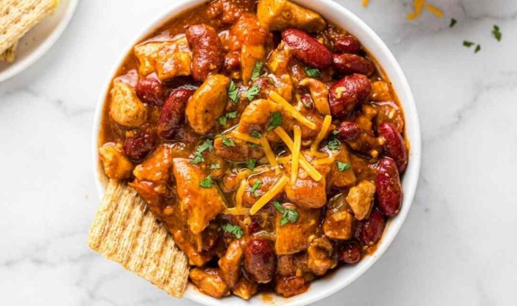 Red chicken chili recipe simmering in a Dutch oven with kidney beans and chicken breast