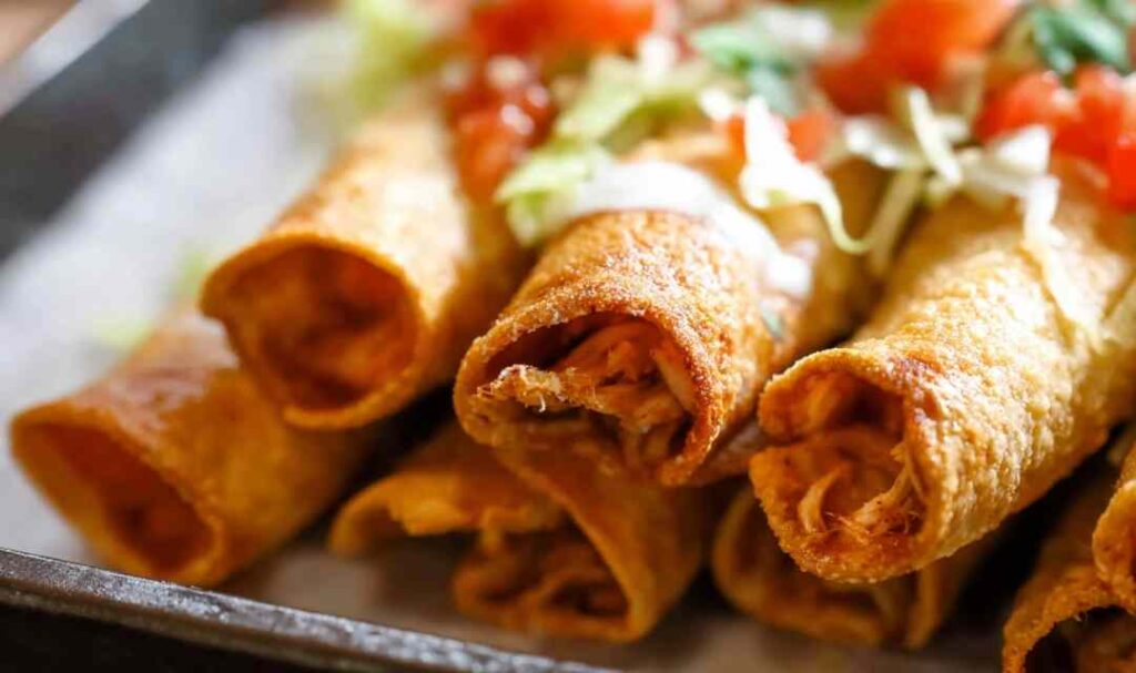 Crispy golden shredded chicken taquitos on a plate with sour cream and salsa dipping sauces