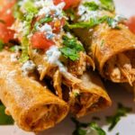 Crispy golden shredded chicken taquitos on a plate with sour cream and salsa dipping sauces