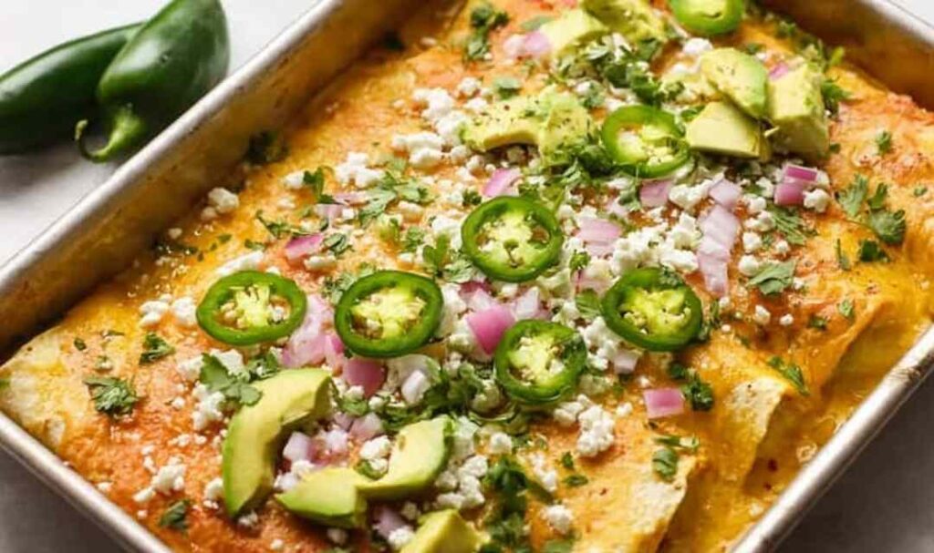 Sour cream chicken enchiladas in a baking dish covered in creamy green chile sauce and melted Monterey Jack cheese