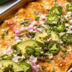 Sour cream chicken enchiladas in a baking dish covered in creamy green chile sauce and melted Monterey Jack cheese