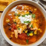 A bowl of Southwest chicken soup topped with crushed tortilla chips, sour cream, and avocado slices